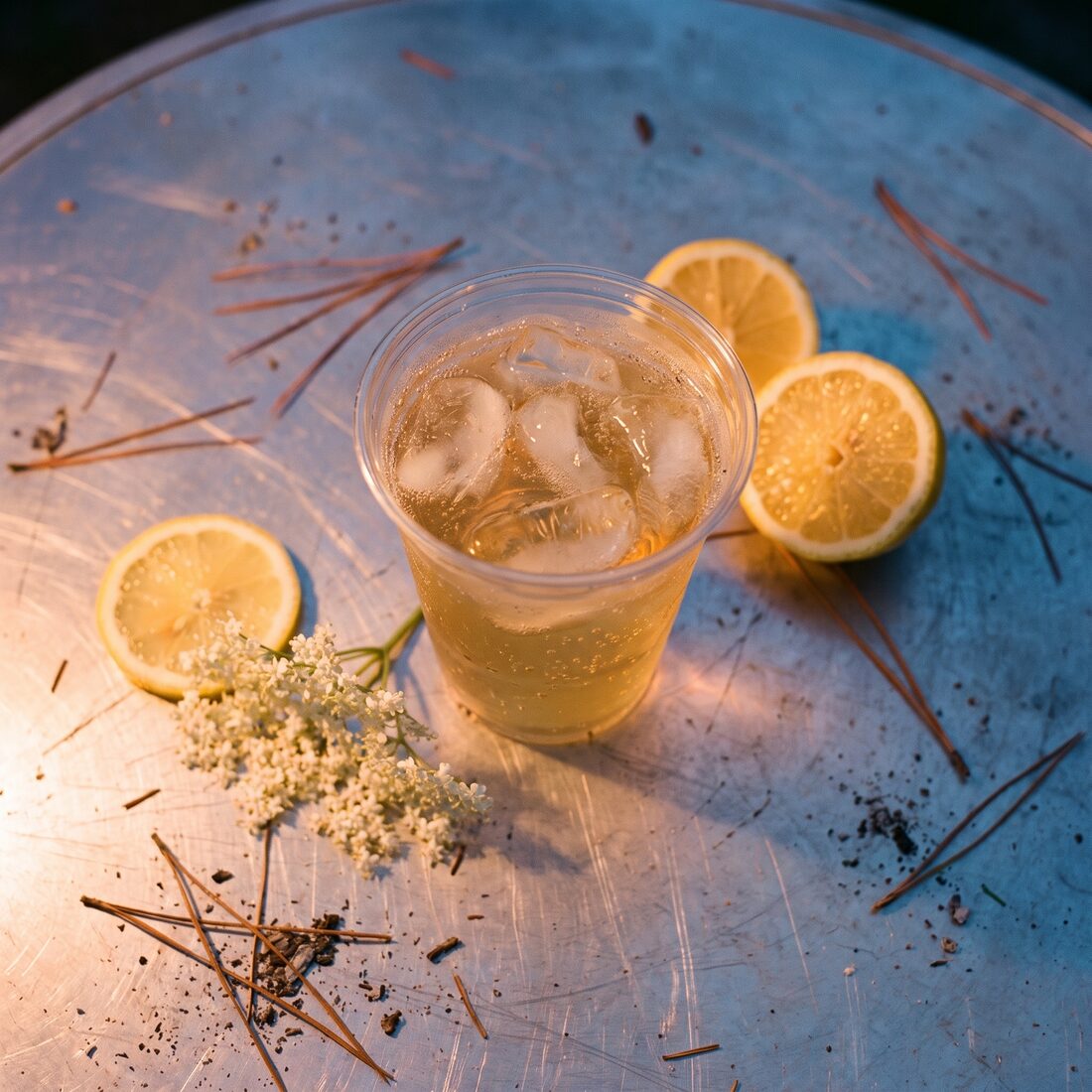 A Limoncello Spritz on a camp table scattered with pine needles and lemon slices