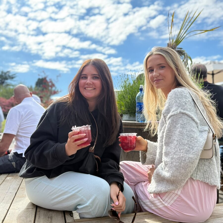 Two guests sitting on a sunny patio deck, each holding a cup of red Sprizzini spritz